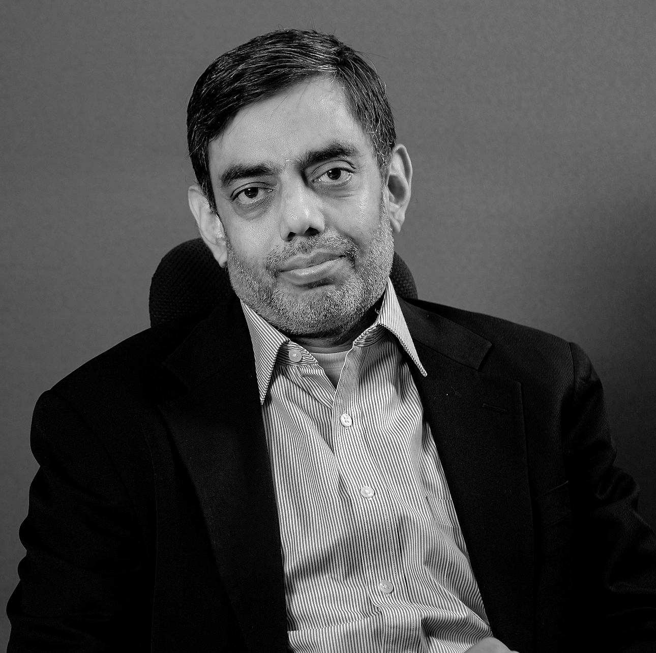 Smiling middle-aged man with light brown hair, wearing round glasses, a white shirt, and a dark blue jacket.