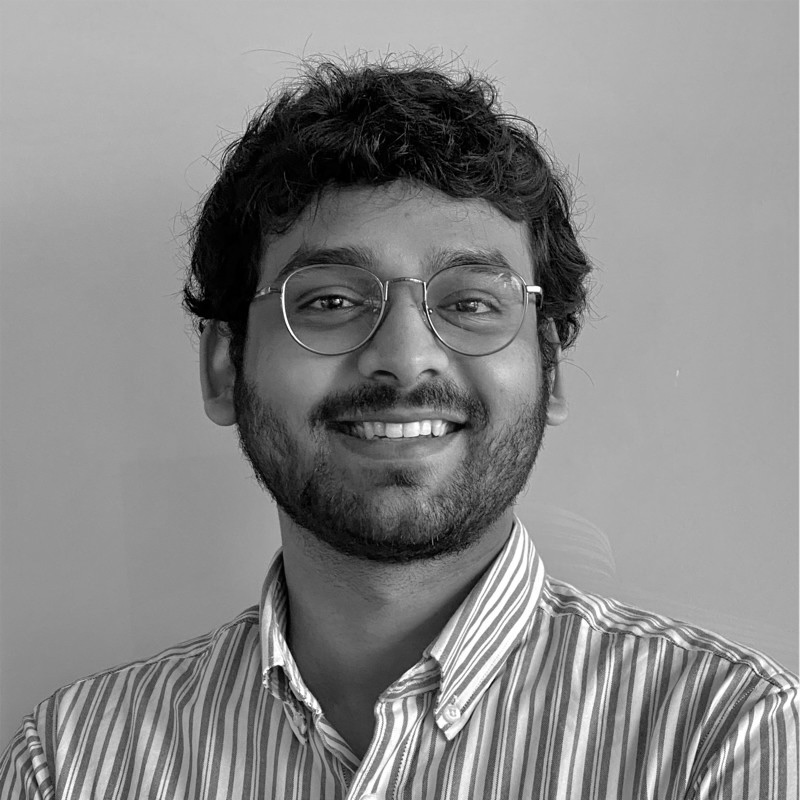 Smiling middle-aged man with light brown hair, wearing round glasses, a white shirt, and a dark blue jacket.