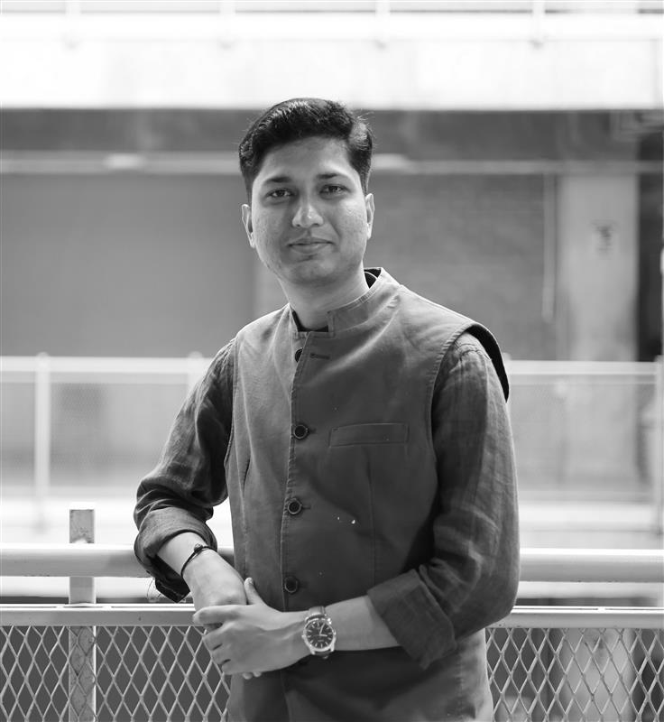 Smiling middle-aged man with light brown hair, wearing round glasses, a white shirt, and a dark blue jacket.