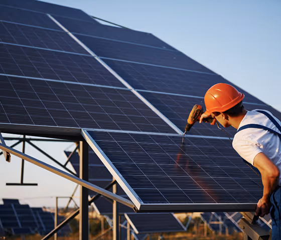 Worker in an orange helmet installing or maintaining solar panels on a sunny day.