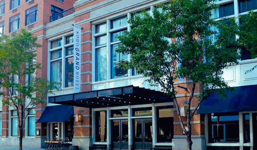Facade of Soho Grand Hotel with glass doors, black awnings, and trees on the sidewalk.