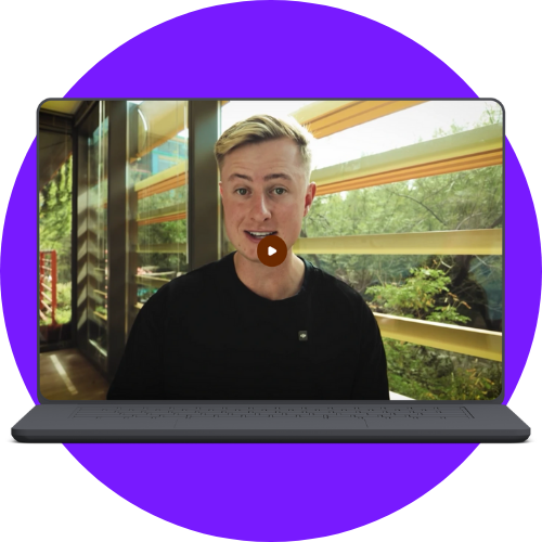 Laptop screen displaying a young man with blond hair and black shirt speaking in a sunlit room with large windows and greenery outside.