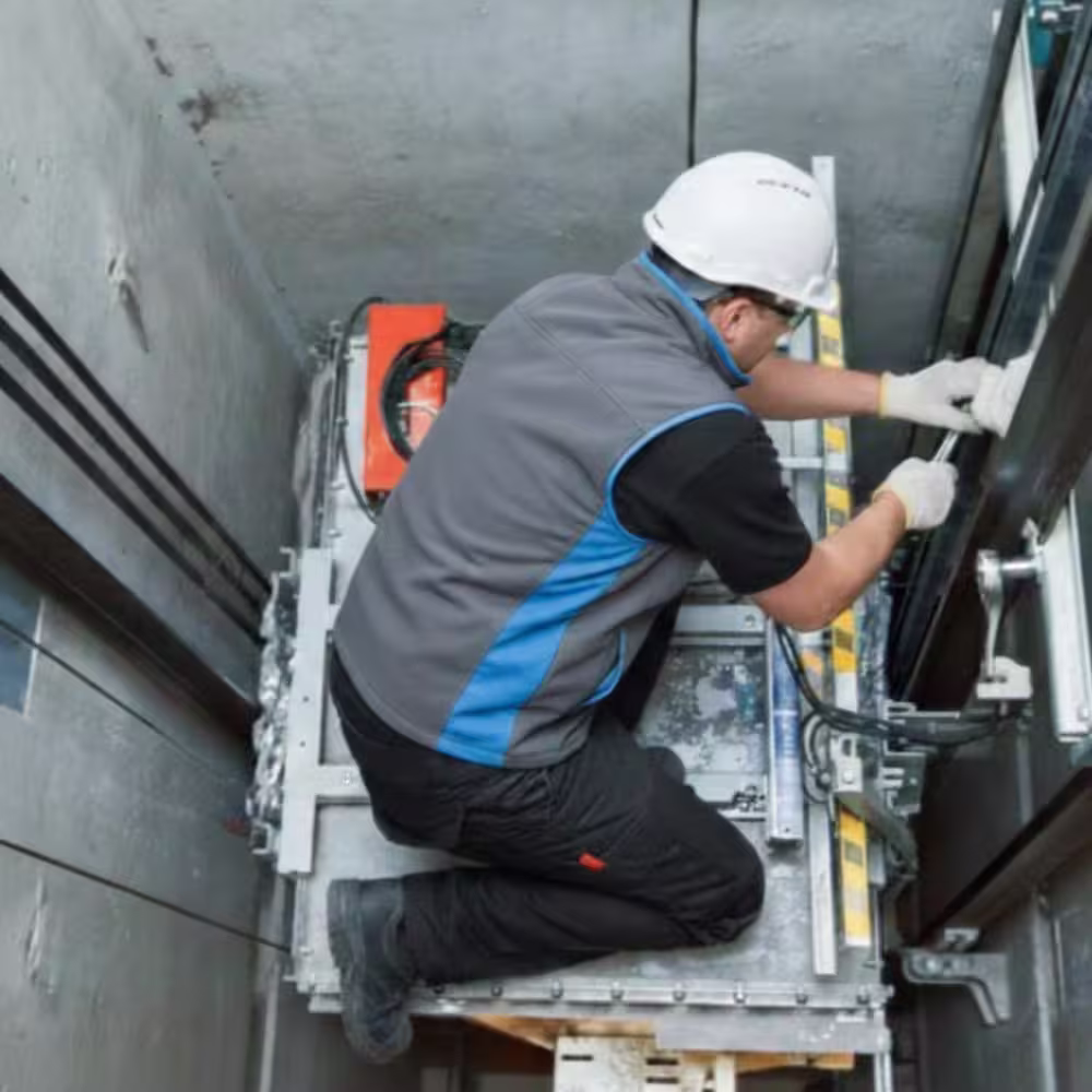 Two construction workers in safety helmets and vests repairing an industrial elevator in a concrete building under construction.