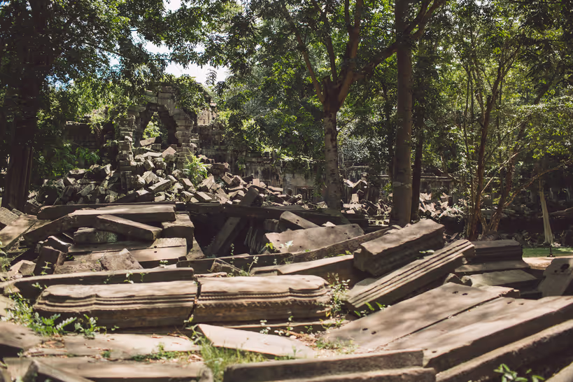 Ancient stone ruins scattered among trees with sunlight filtering through the forest canopy.