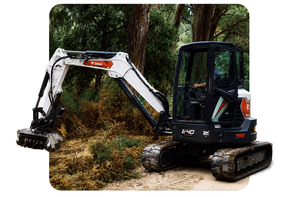 Bobcat E40 compact excavator with a mulching attachment clearing vegetation in a wooded area.