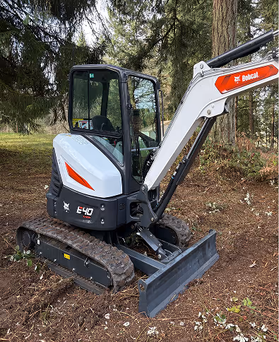 White and black Bobcat E40 compact excavator parked on a forest floor with trees in the background.