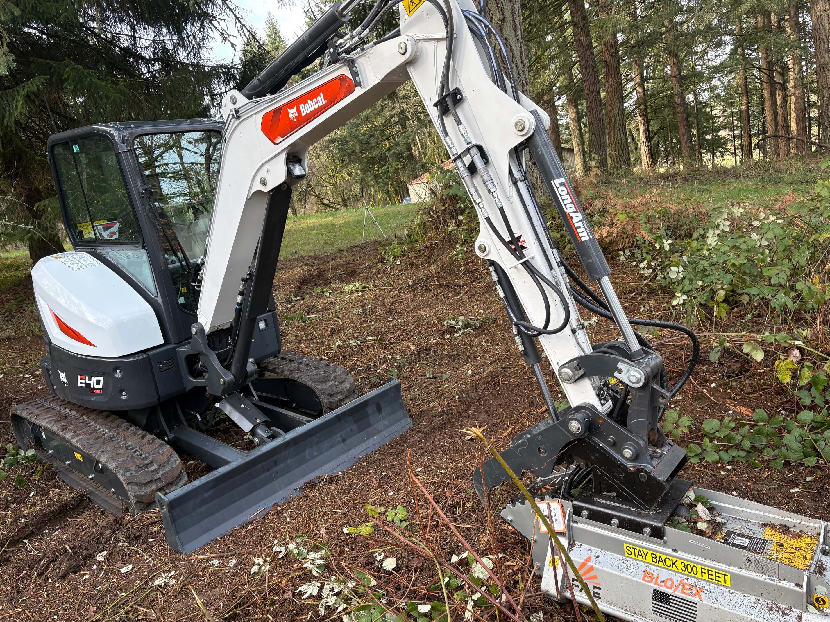 Bobcat E40 excavator with LongArm attachment clearing brush in a forested area.