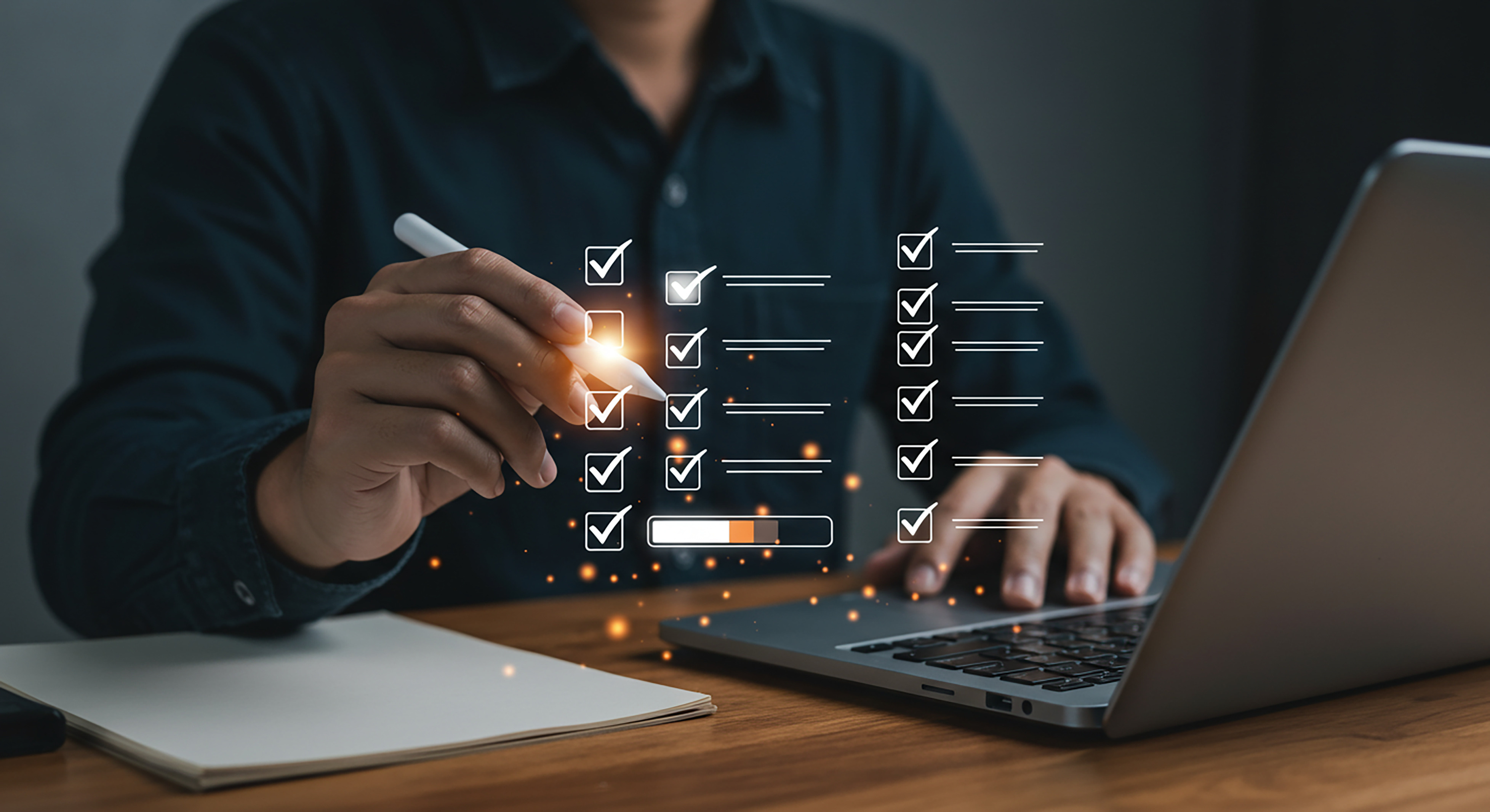 Person using a stylus to check off items on a virtual checklist next to a laptop on a desk.