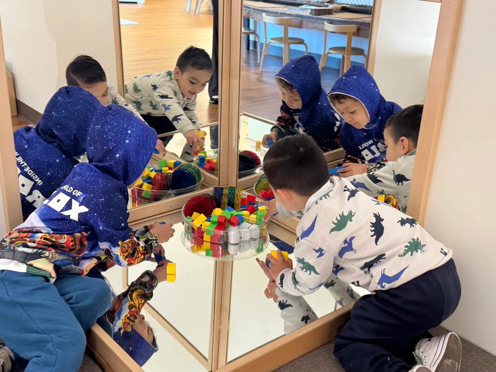 Two young boys playing with colorful blocks in front of a corner mirror in a classroom.