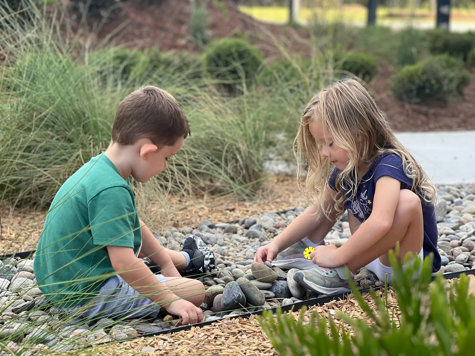 A boy and a girl sitting on rocks outdoors, playing and arranging stones together.