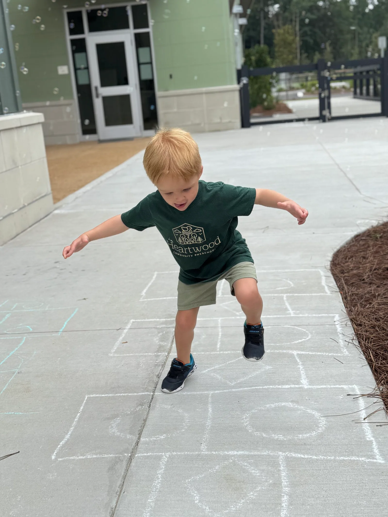 Young child playing hopscotch on a concrete sidewalk outside a building.