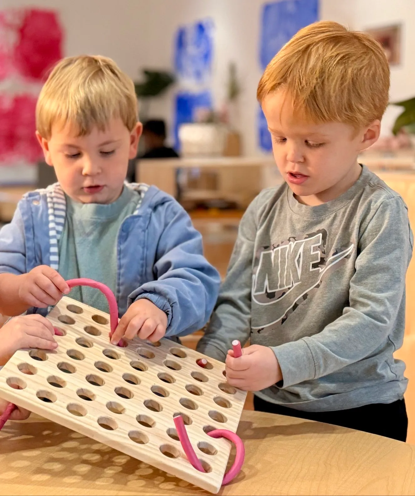 Two young boys playing with a wooden pegboard toy at a table indoors.