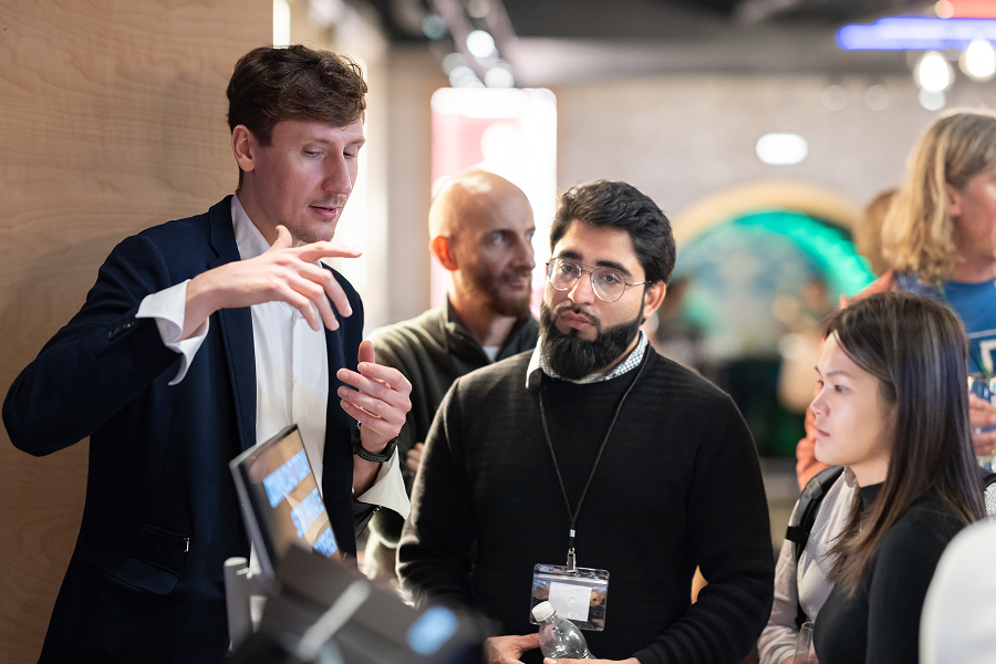 Group of MLOps attendees in suits and lanyards discussing near laptops and drinks