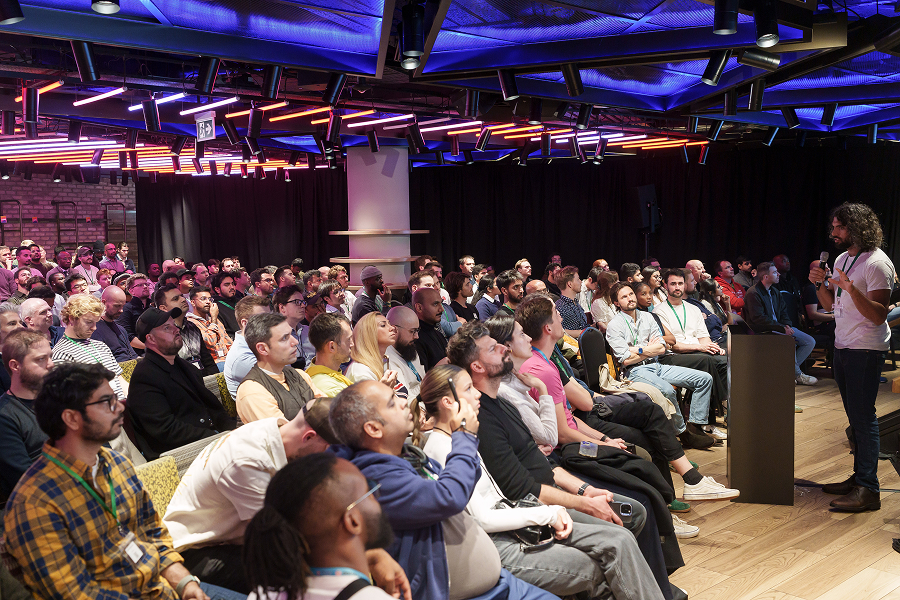 Large audience attending an MLOps conference presentation under neon-lit ceiling