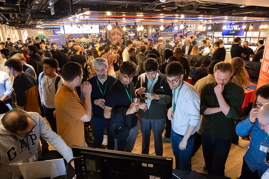 Diverse group of MLOps professionals with lanyards gathered around a screen at a crowded conference booth