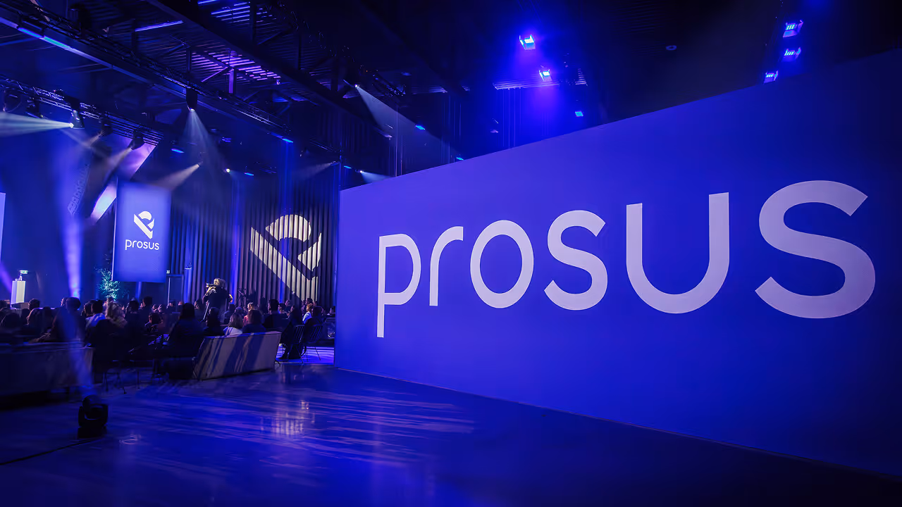 Prosus company name in large white letters on a blue stage backdrop with spotlights and audience