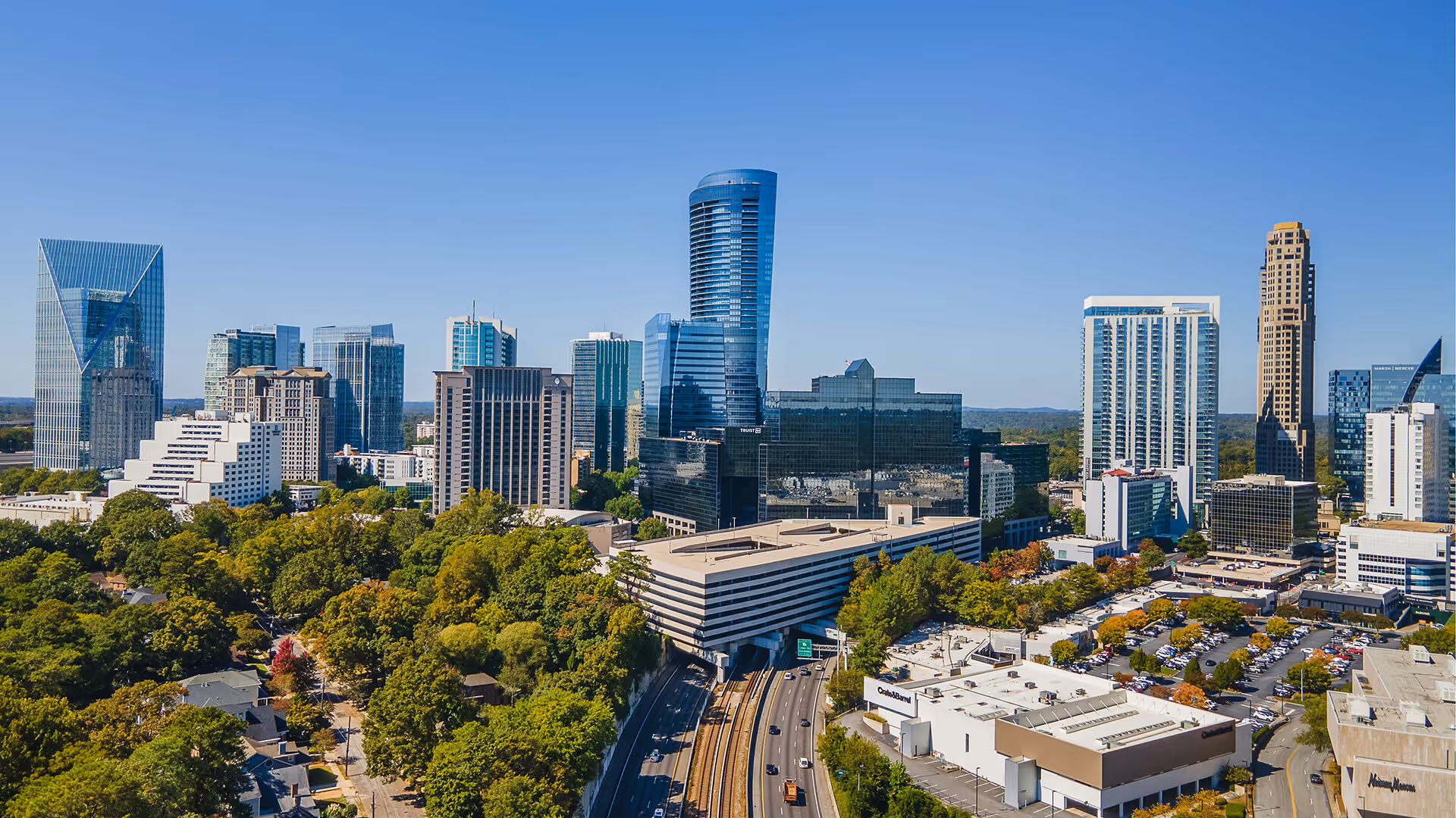 Atlanta skyline featuring tall modern skyscrapers, green trees, and highways under a clear blue sky