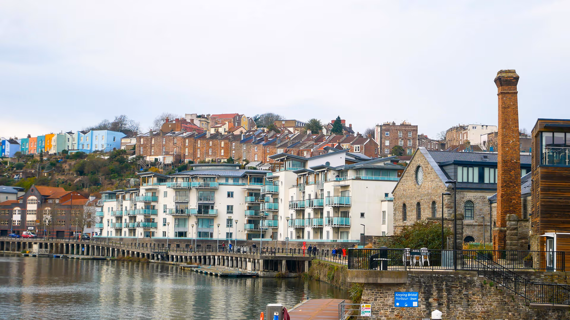 Bristol harbor with colorful terraced houses on hills, modern apartments, and chimney along the river