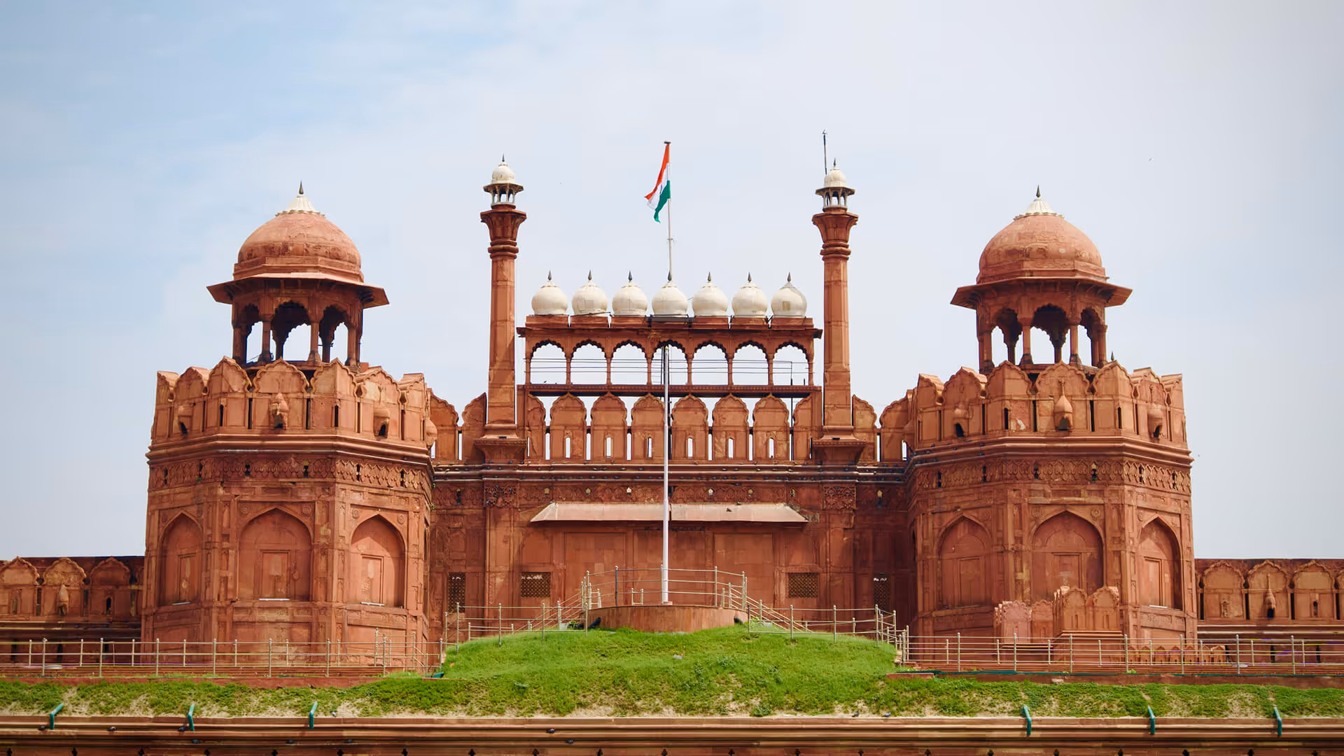 Delhi's red sandstone Lahori Gate at Red Fort with minarets, Indian flag, and green lawns