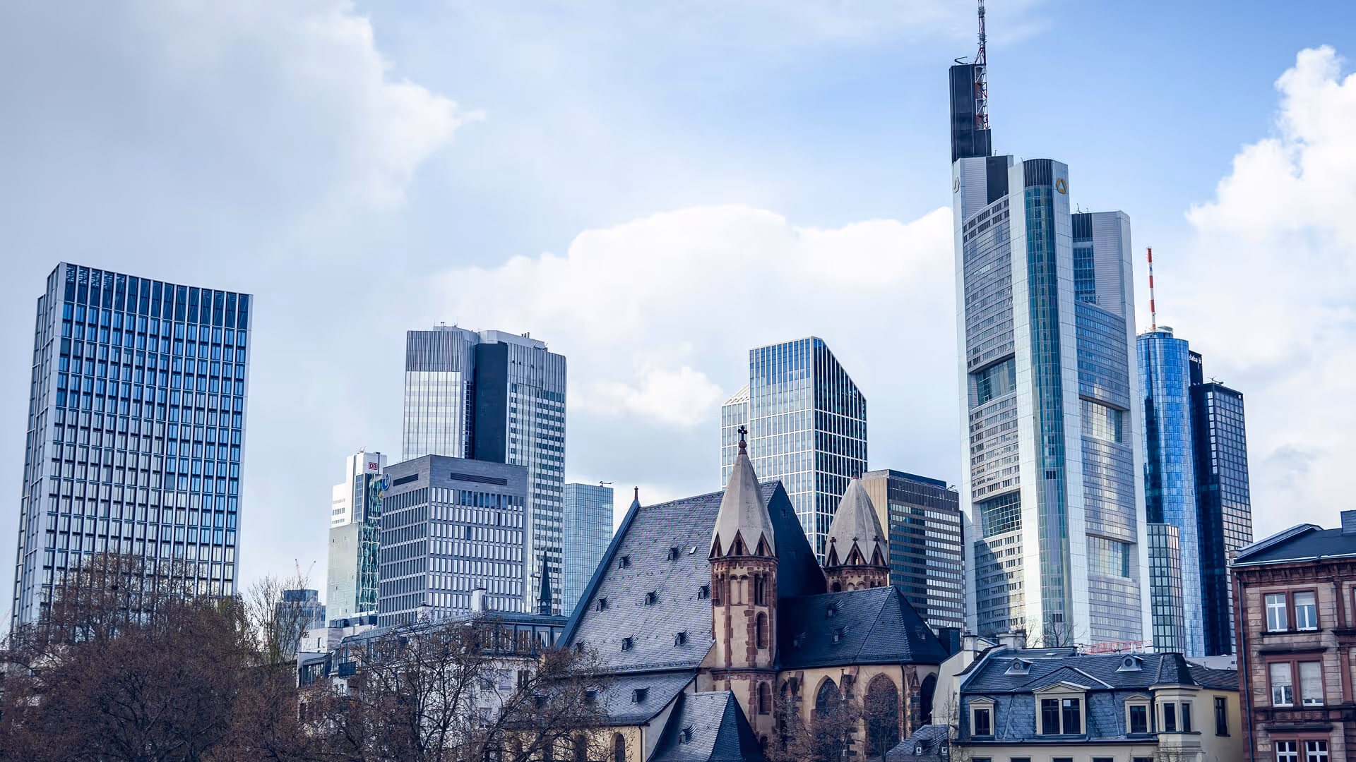 Frankfurt skyline with Commerzbank Tower, modern high-rises, and historic church steeple amid trees