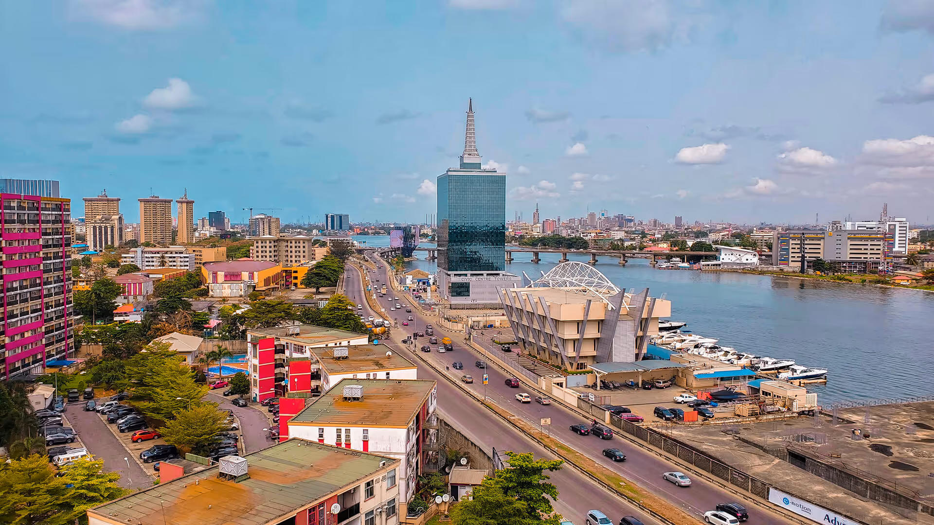 Lagos skyline with tall green Pinnacle Tower, high-rises, boats, and highway along the lagoon