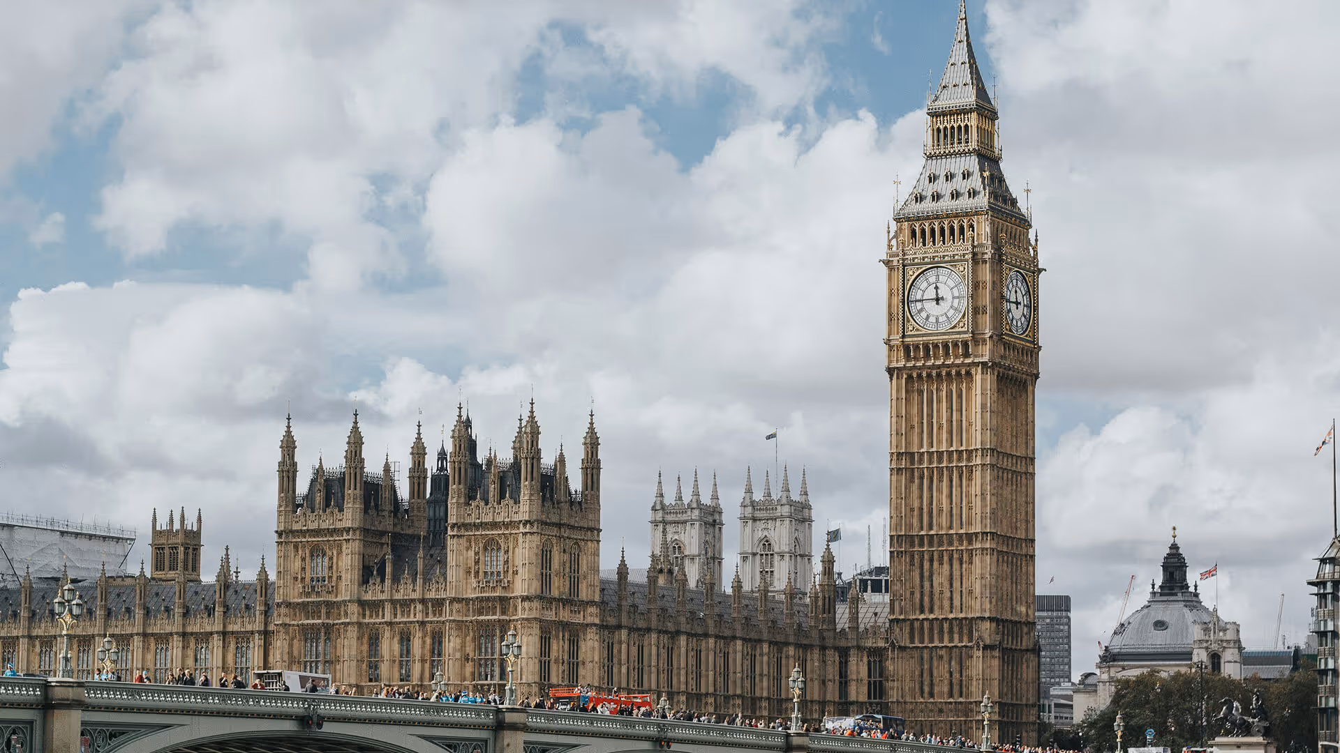 London's Big Ben clock tower and Houses of Parliament Gothic spires beside River Thames under partly cloudy skies
