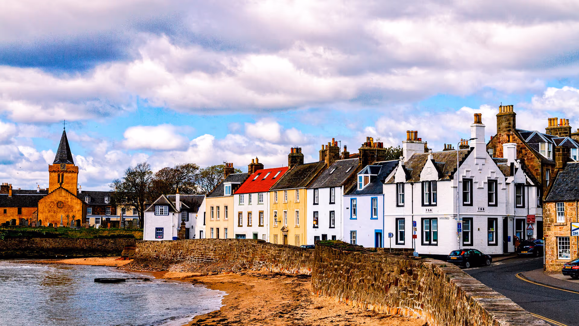 Colorful Georgian houses lining the harbor shore with orange church tower in Scottish coastal village