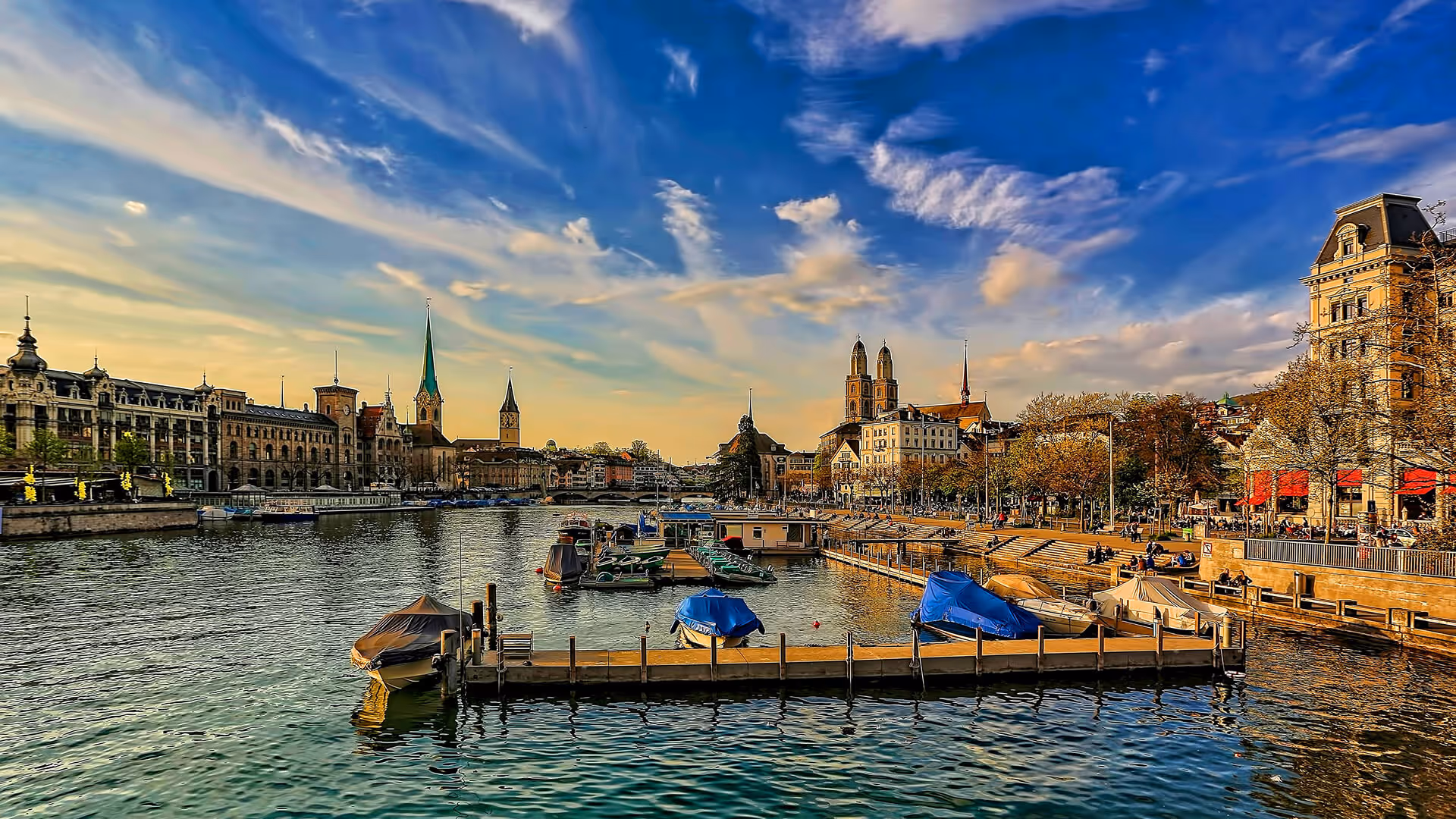 Zurich waterfront with church spires, boats on Limmat River, and elegant buildings at golden hour