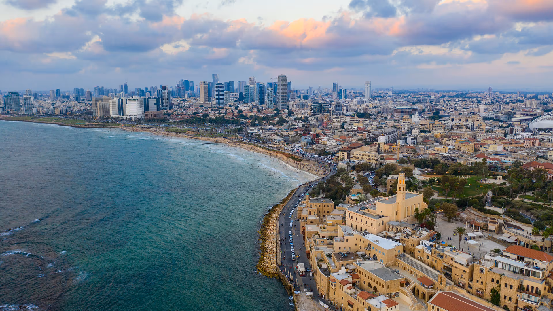 Tel Aviv skyline with modern towers, Jaffa old town minaret, beach promenade, and Mediterranean Sea at dusk