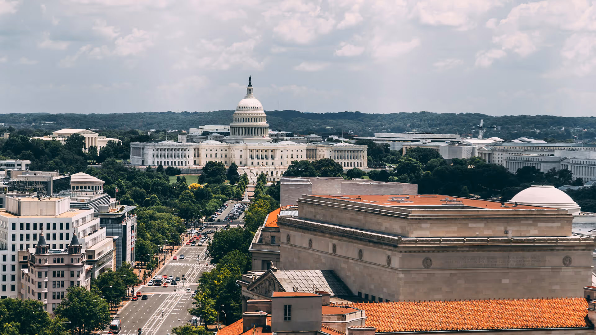 Washington DC U.S. Capitol dome with surrounding monuments, green trees, and urban avenues