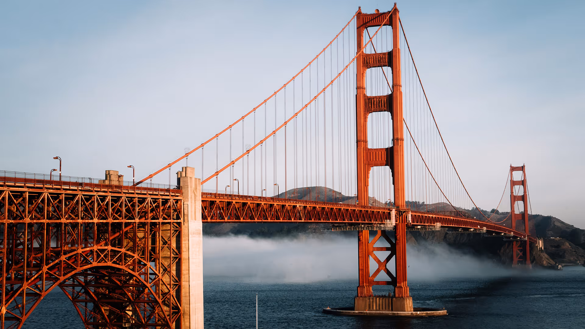 San Francisco Golden Gate Bridge in golden light with fog rolling over blue bay water