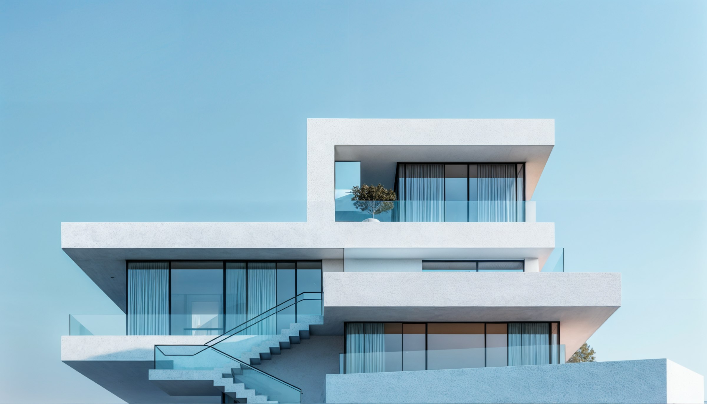 Modern white multi-level house with large glass windows, glass railings, and exterior stairs under a clear blue sky.