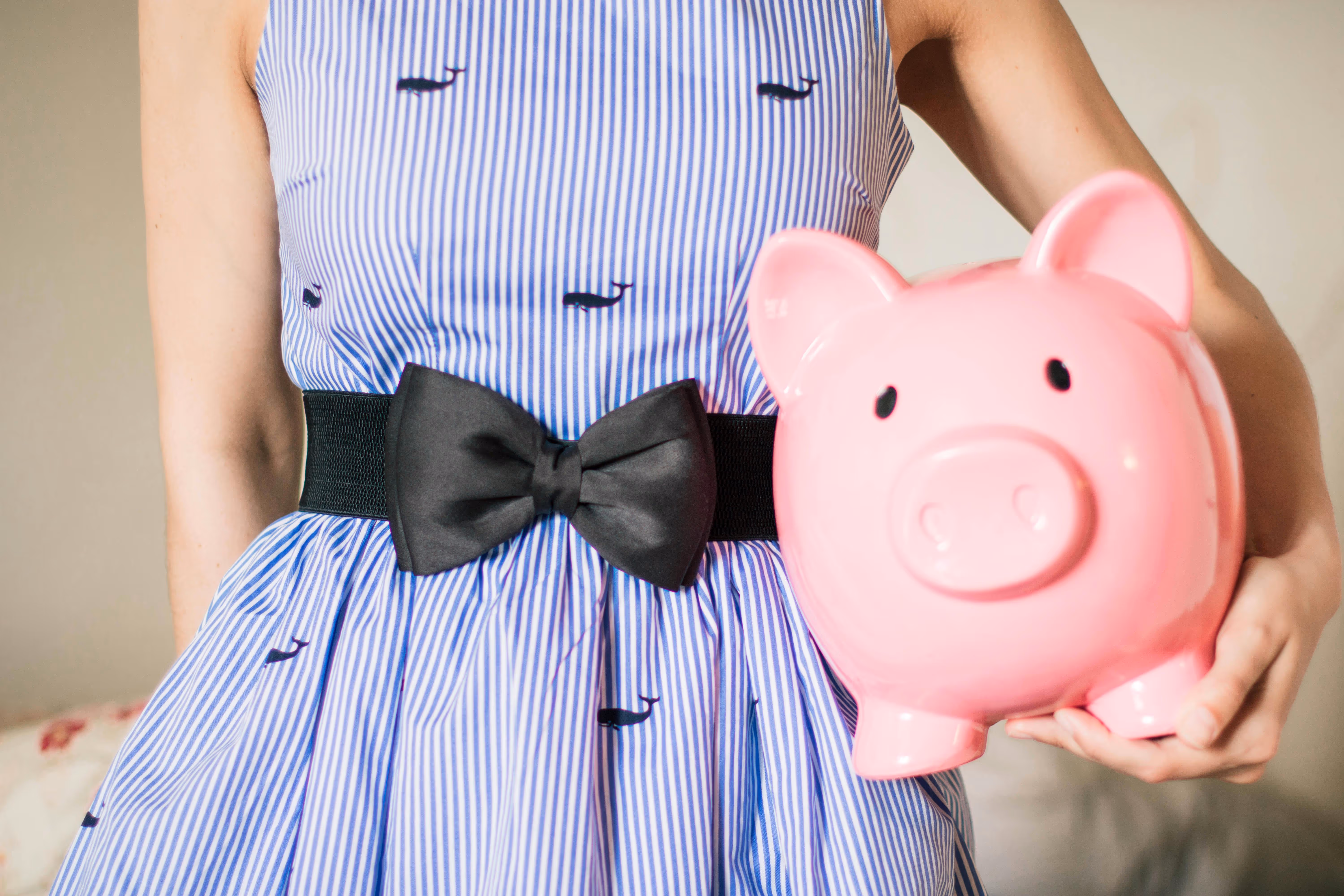 A lady in a patterned dressed holding a pink piggie bank