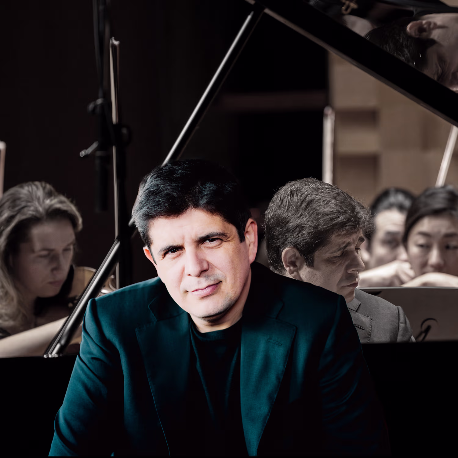 A Javier Perianes in a dark jacket poses confidently in front of a grand piano, his face lit against a darker background. Reflected in the piano lid, he appears again while an orchestra with string players performs behind him, creating a layered, dramatic