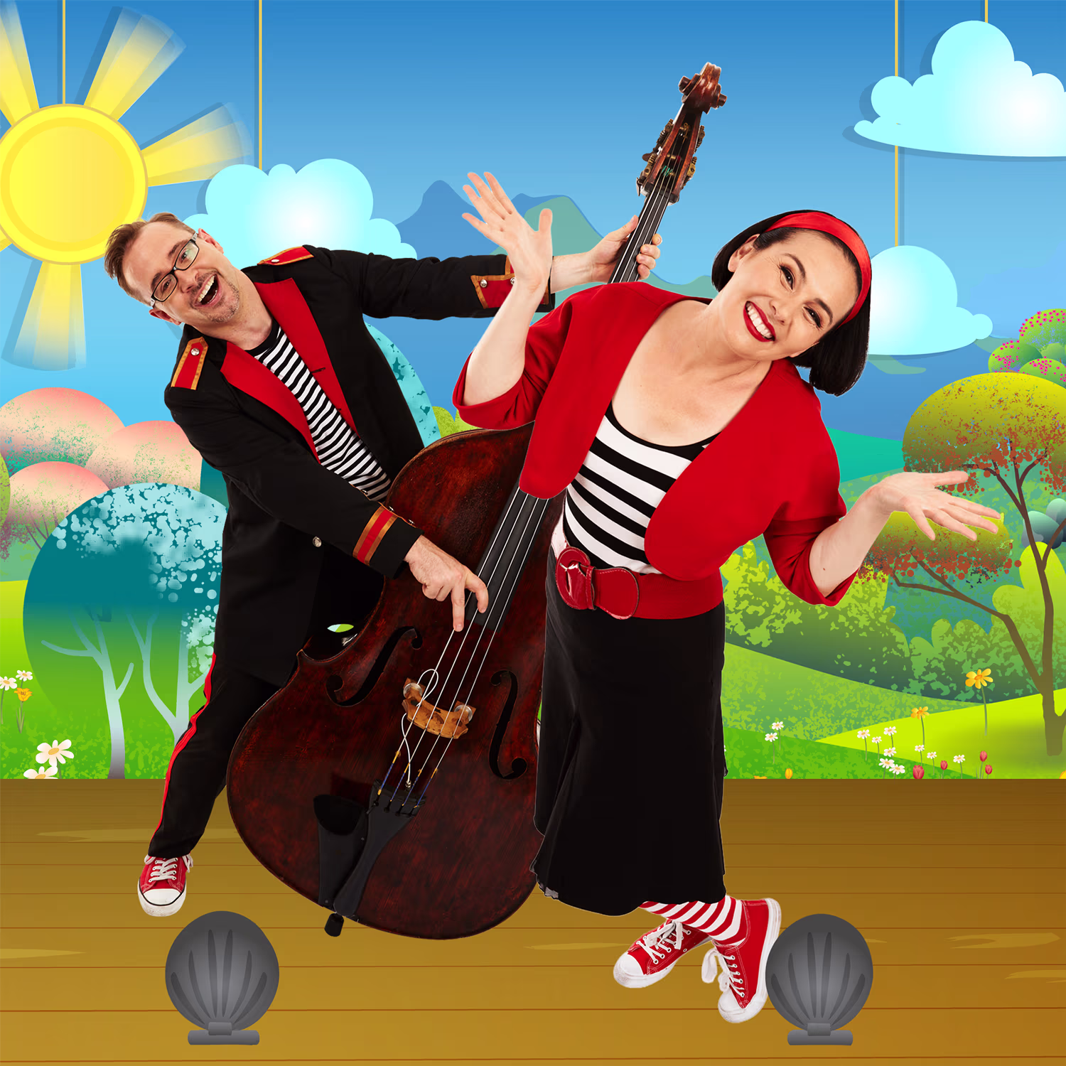Two performers Lah-Lah and Buzz the Bandleader dressed in matching black, red, and white outfits stand on a colorful stage with a cartoon-style outdoor backdrop featuring a bright sun, clouds, trees, and hills. Buzz the Bandleader is playing a double bass