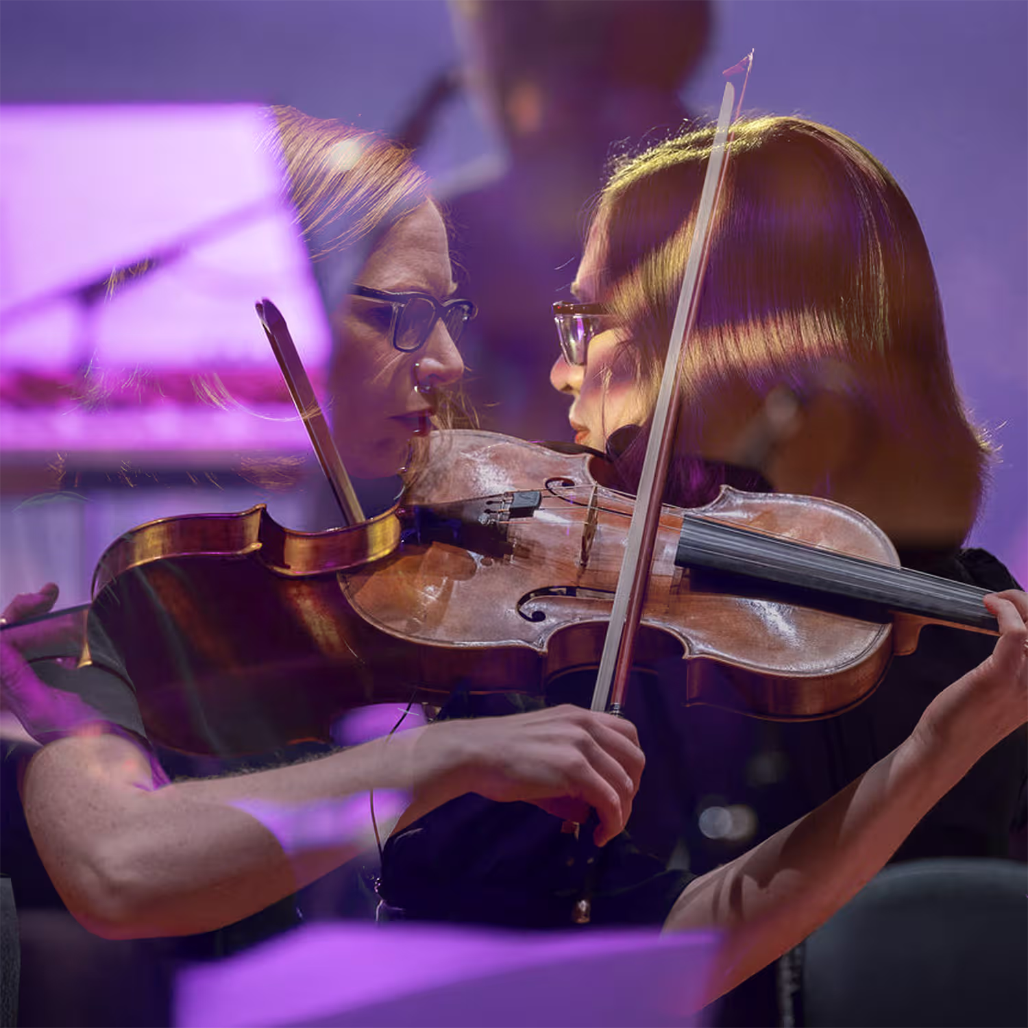 Double exposure photograph of a violinist, with two overlapping views creating a mirrored effect. The background features soft, blurred purple and pink tones, giving the image an artistic and dreamy ambiance.