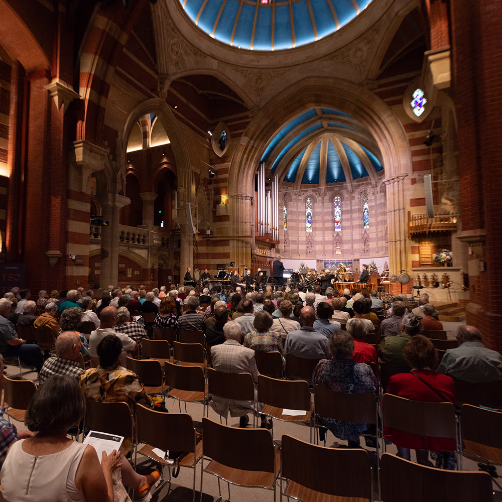 An audience watches a musical performance inside a stained glass church.