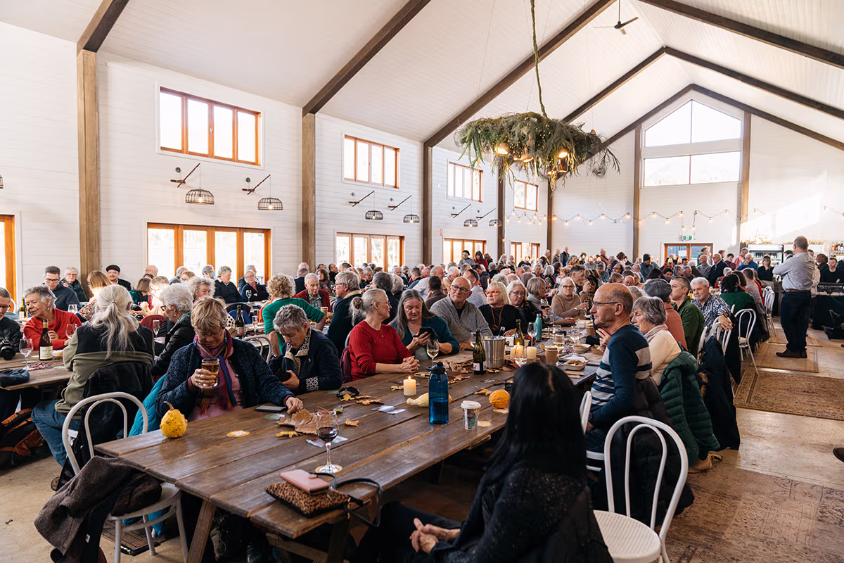 A hall filled with people eating, drinking and laughing at long tables.