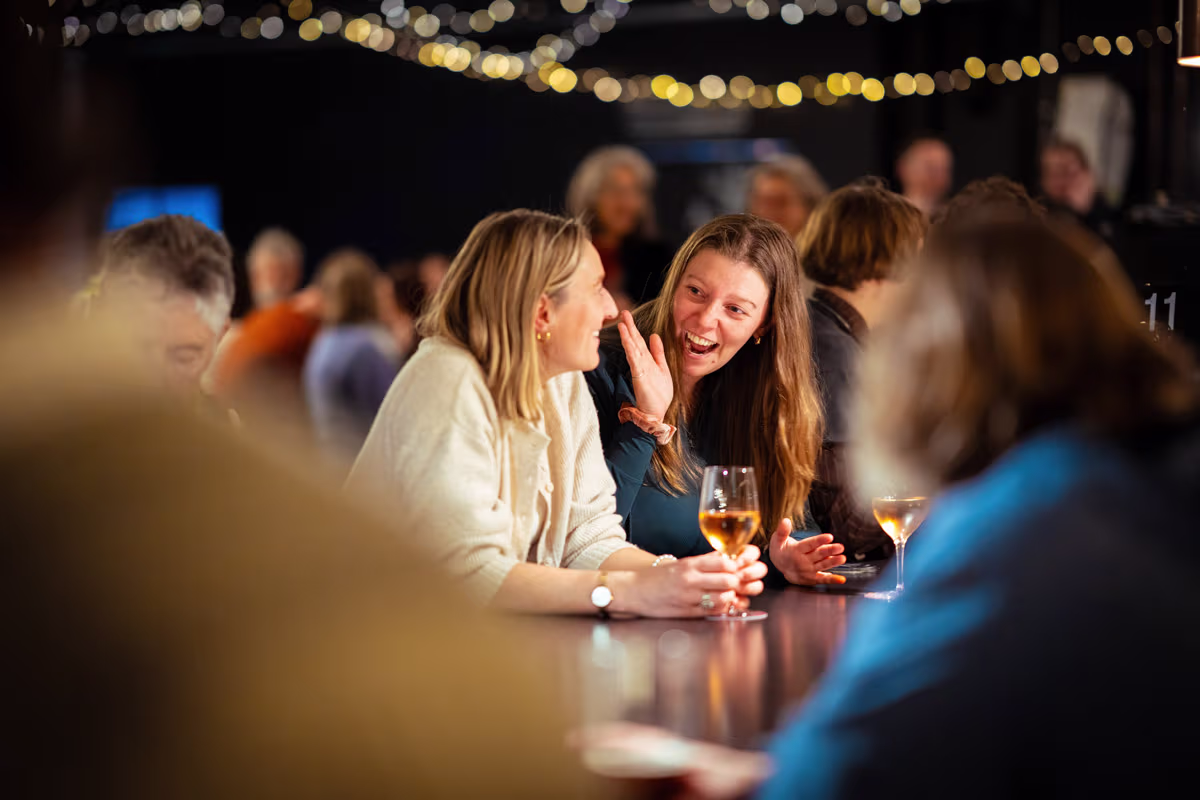 Two women drinking wine and smiling at a concert.
