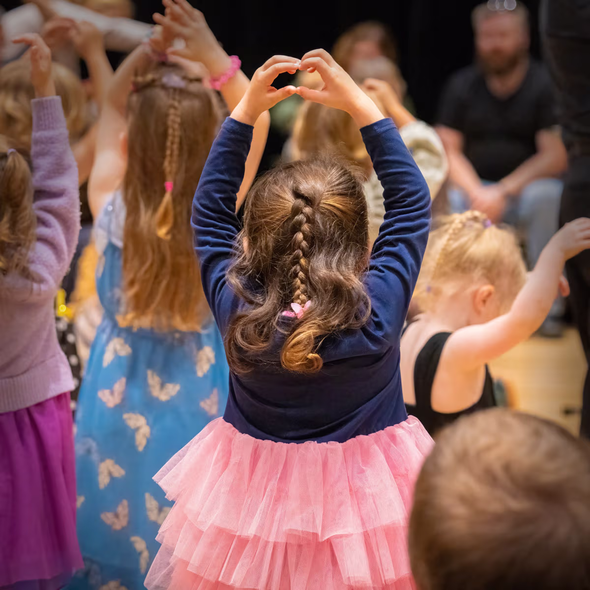 A little girl in a tutu raising her arms like a ballerina.
