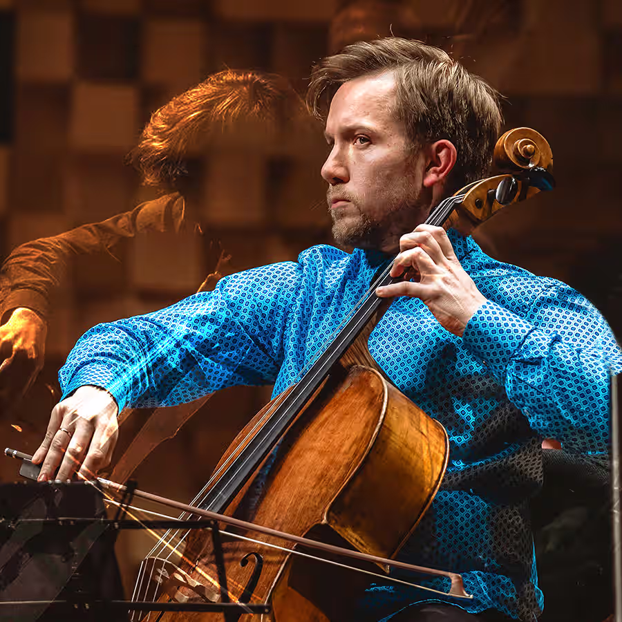A man playing the cello in a blue shirt.