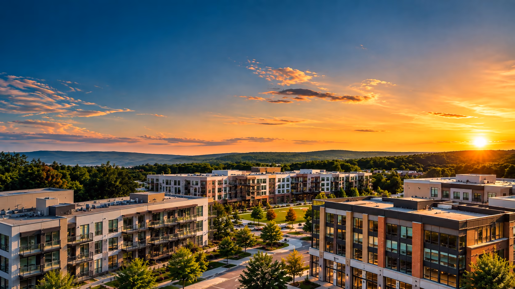 Modern apartment buildings with tree-lined streets at sunset and hills in the background.