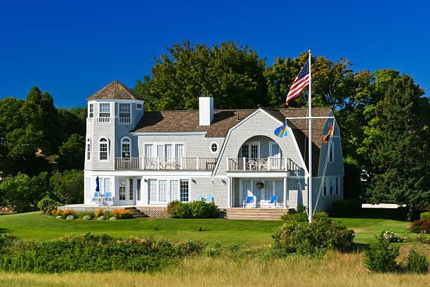 An image of a luxury Home in Hyannis, Cape Cod with 3 flags on a flag pole and patio chairs during the daytime.