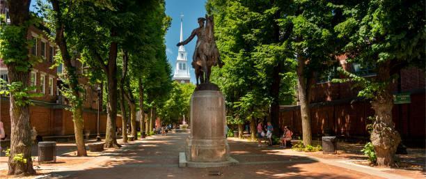 An image of a statue of Paul Revere on the historic Boston Freedom Trail lined with trees with the Old North Church steeple in behind.