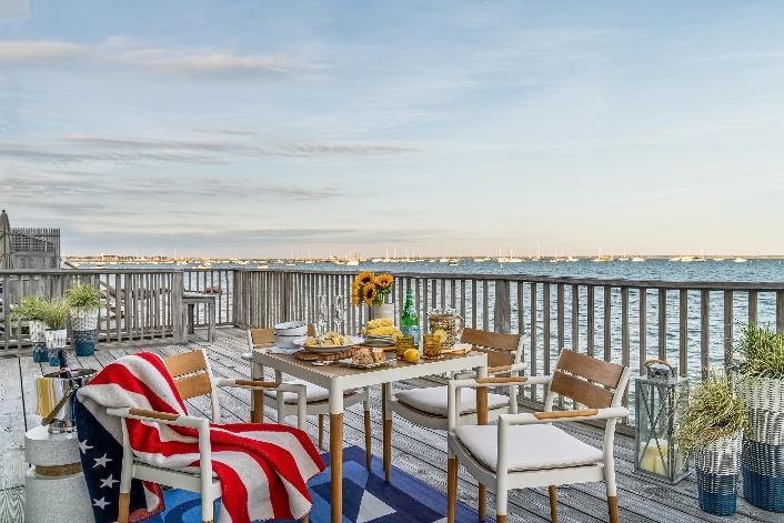 An image of Westminster Teak Bloom Dining Set on outdoor wood deck overlooking the ocean and city skyline in the background.