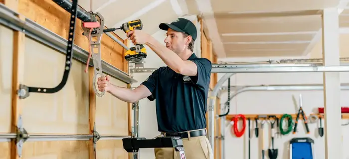 Technician using a power drill and a large wrench to repair a garage door inside a garage.