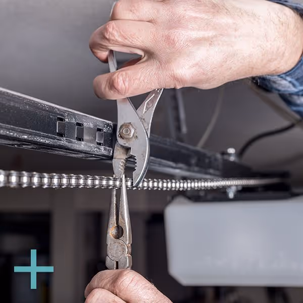 Hands using two pairs of pliers to adjust or fix a metal chain on a black mechanical frame.