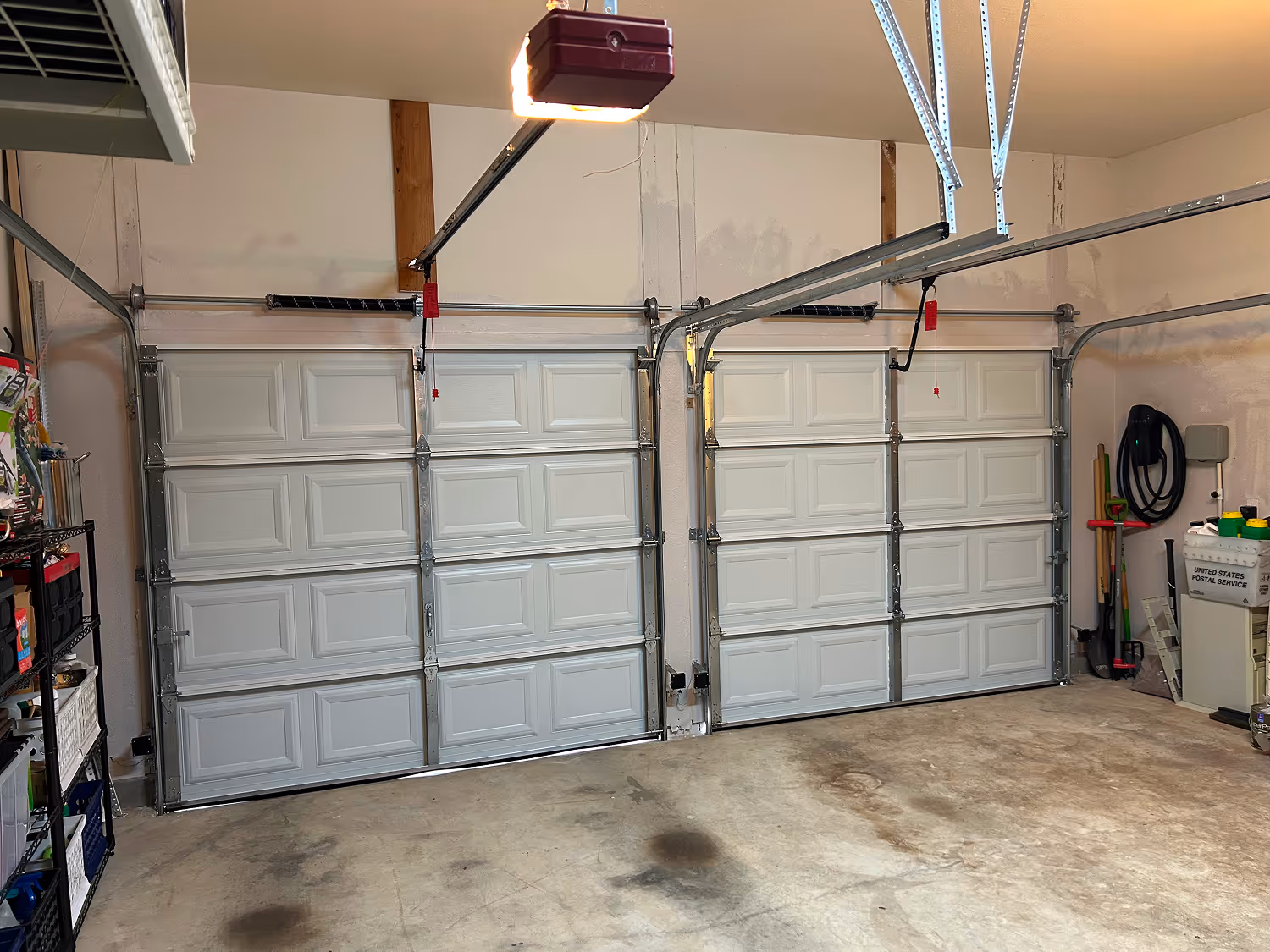Interior of a clean garage with two closed white sectional garage doors and various tools and storage shelves along the walls.