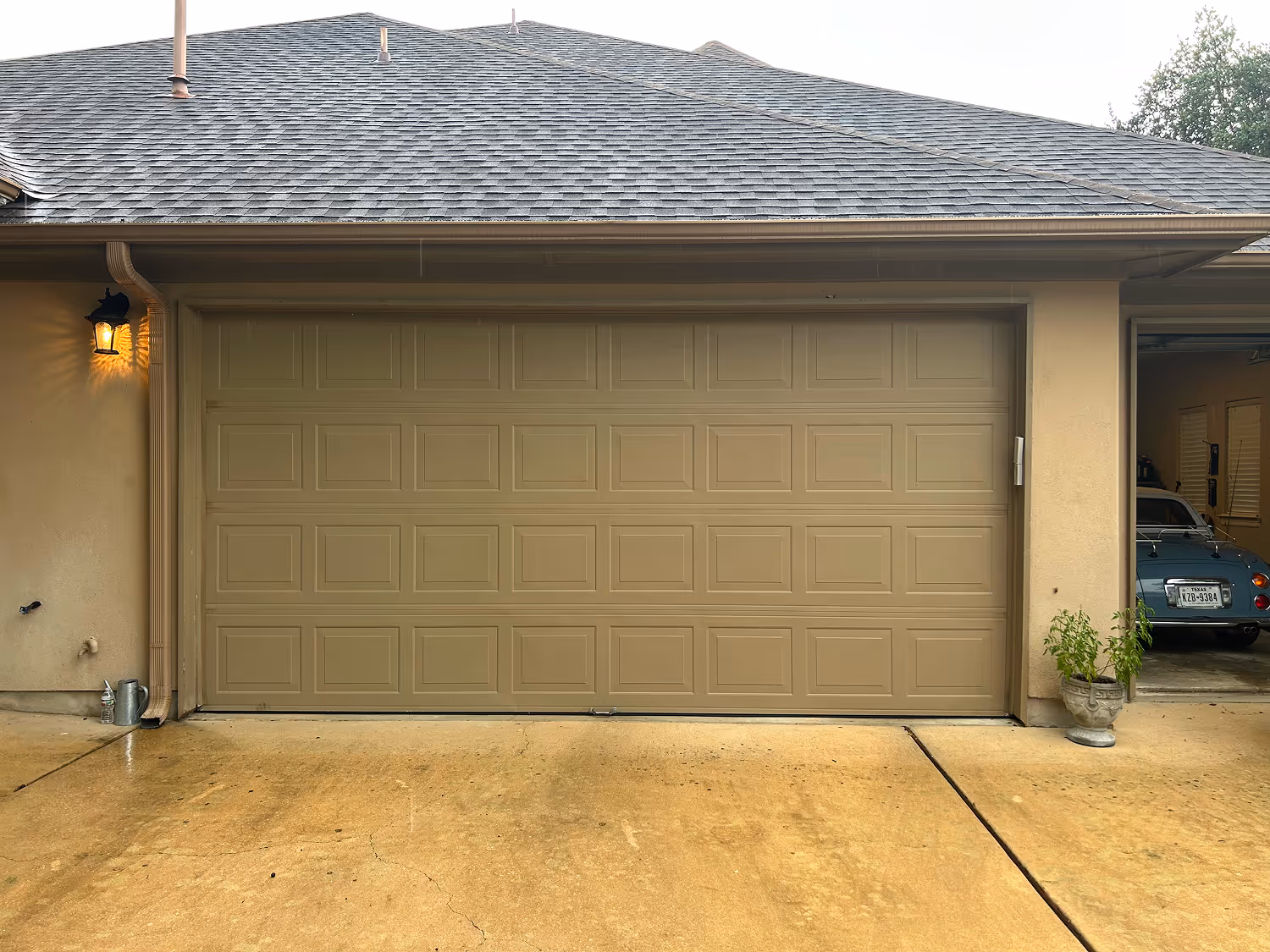 Closed beige garage door with panels and an adjacent open garage showing a vintage blue car inside.