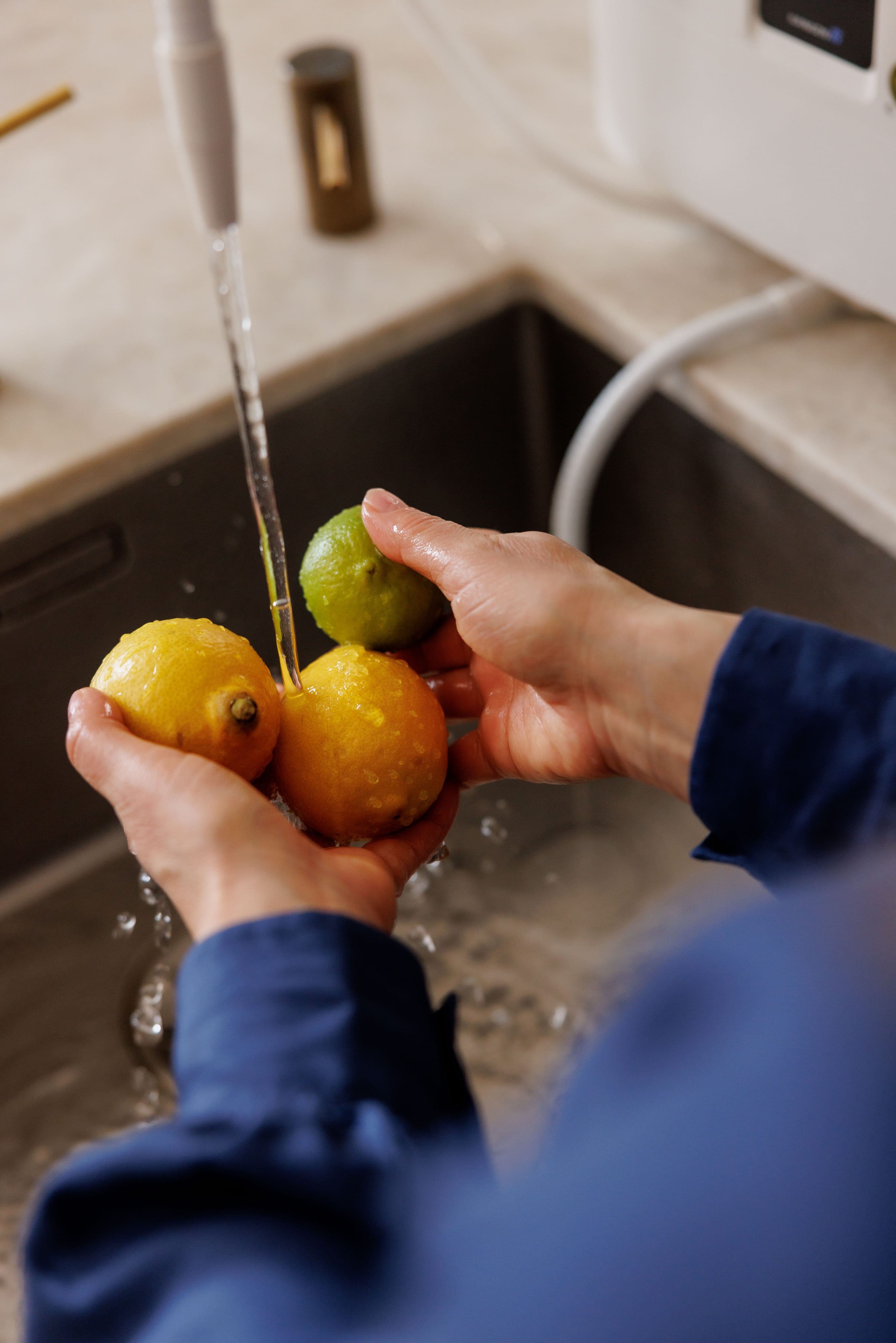 Iemand die twee citroenen en een limoen onder stromend water in een gootsteen wast.